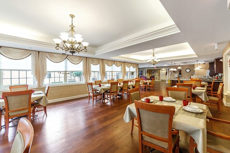 An elegant dining area with chandeliers, neatly arranged tables and chairs, featuring warm wood flooring.