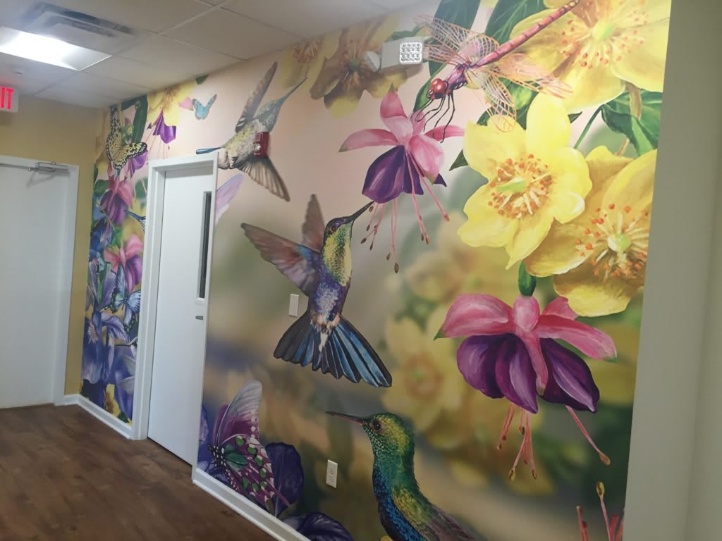 A vibrant mural featuring colorful flowers and hummingbirds on an indoor wall.