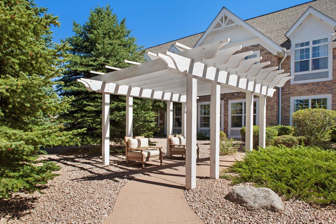 A serene outdoor seating area with a white pergola in a landscaped garden.