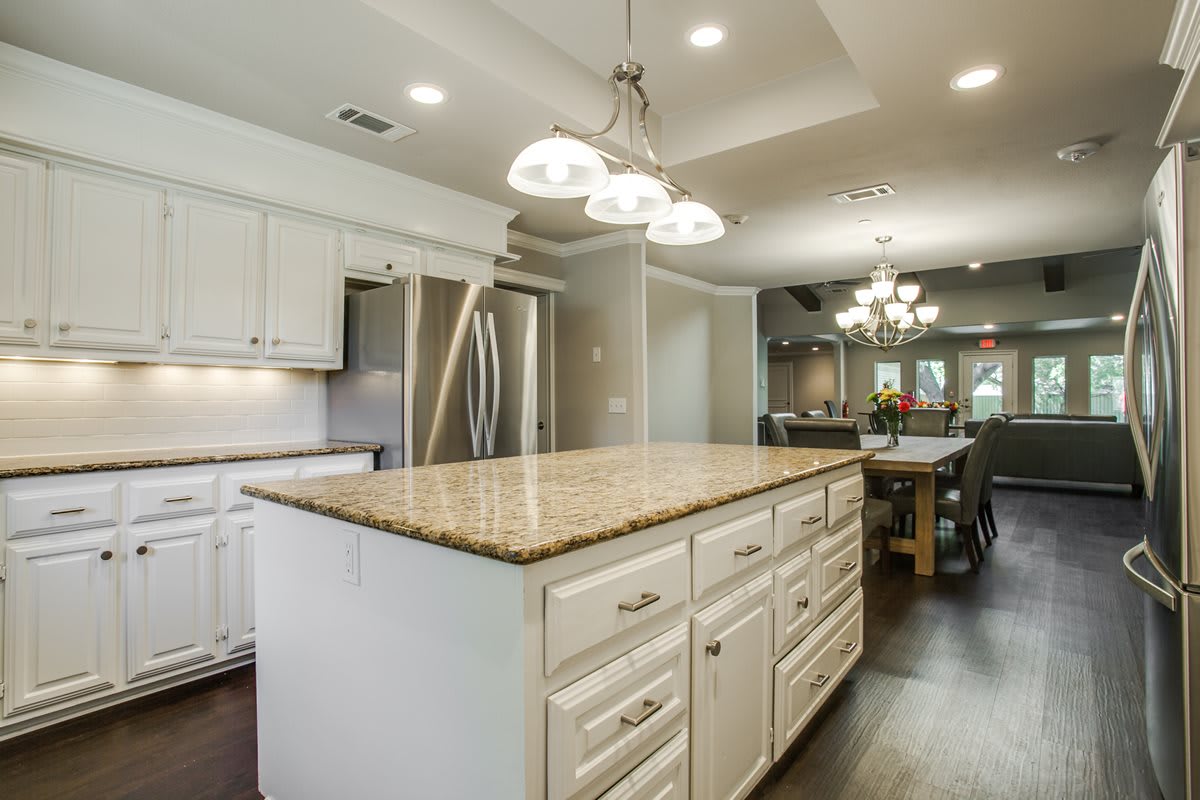 A modern kitchen with a large island and granite countertops, featuring elegant lighting and spacious cabinetry.