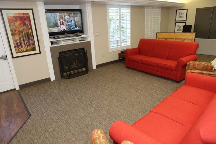 A cozy living room with red couches, a television above the fireplace, and carpeted flooring.