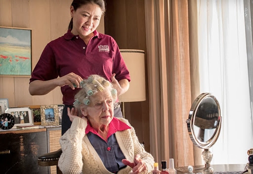 A caregiver lovingly styles the hair of an elderly woman, showcasing the importance of companionship and care in senior living.