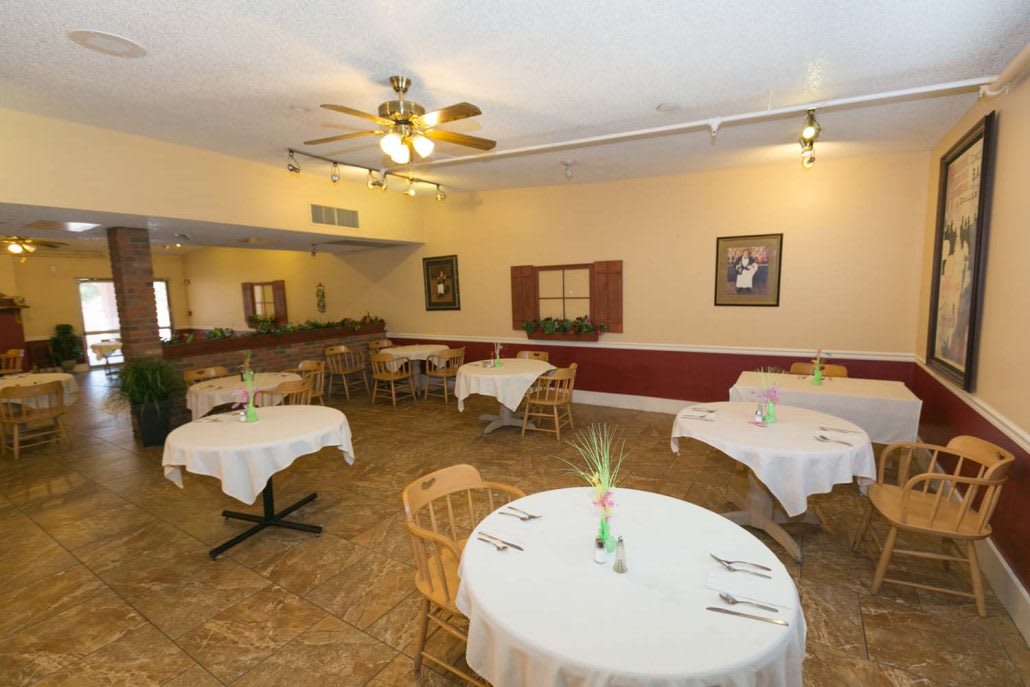 An empty dining area with round tables and wicker chairs, set for customers.