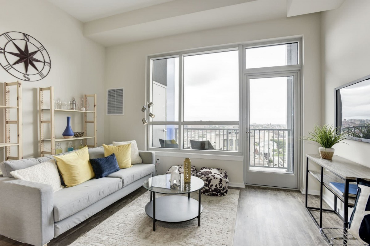 A modern living room with a stylish sofa, decorative cushions, and a round coffee table, featuring large windows for natural light.