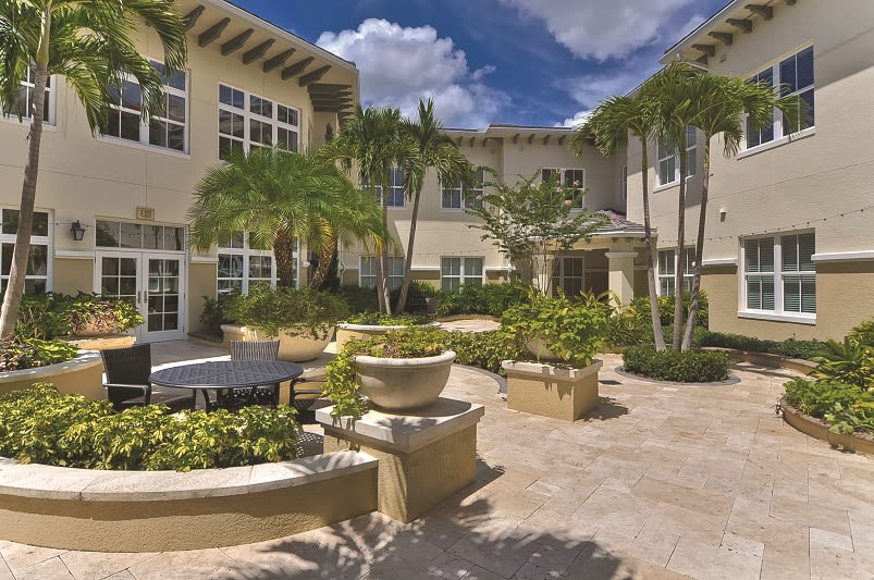A beautifully landscaped courtyard with potted plants and palm trees in front of a residential building.