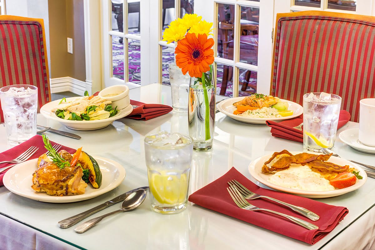 A beautifully set dining table with meals, utensils, and a floral centerpiece.