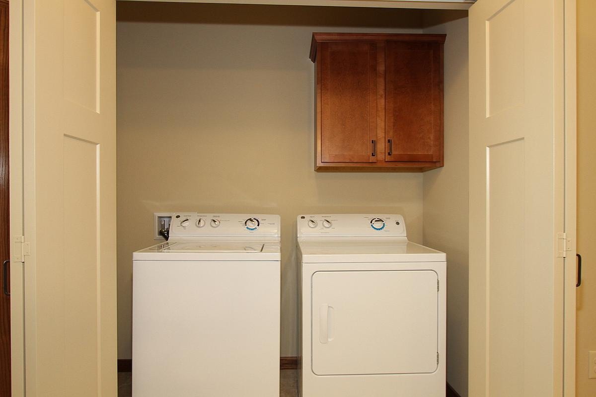 A compact laundry room with a washer and dryer beneath a wooden storage cabinet.