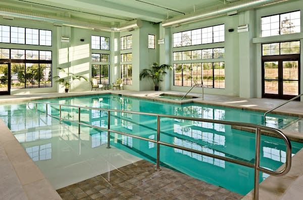 A sunlit indoor swimming pool surrounded by large windows and modern architecture.