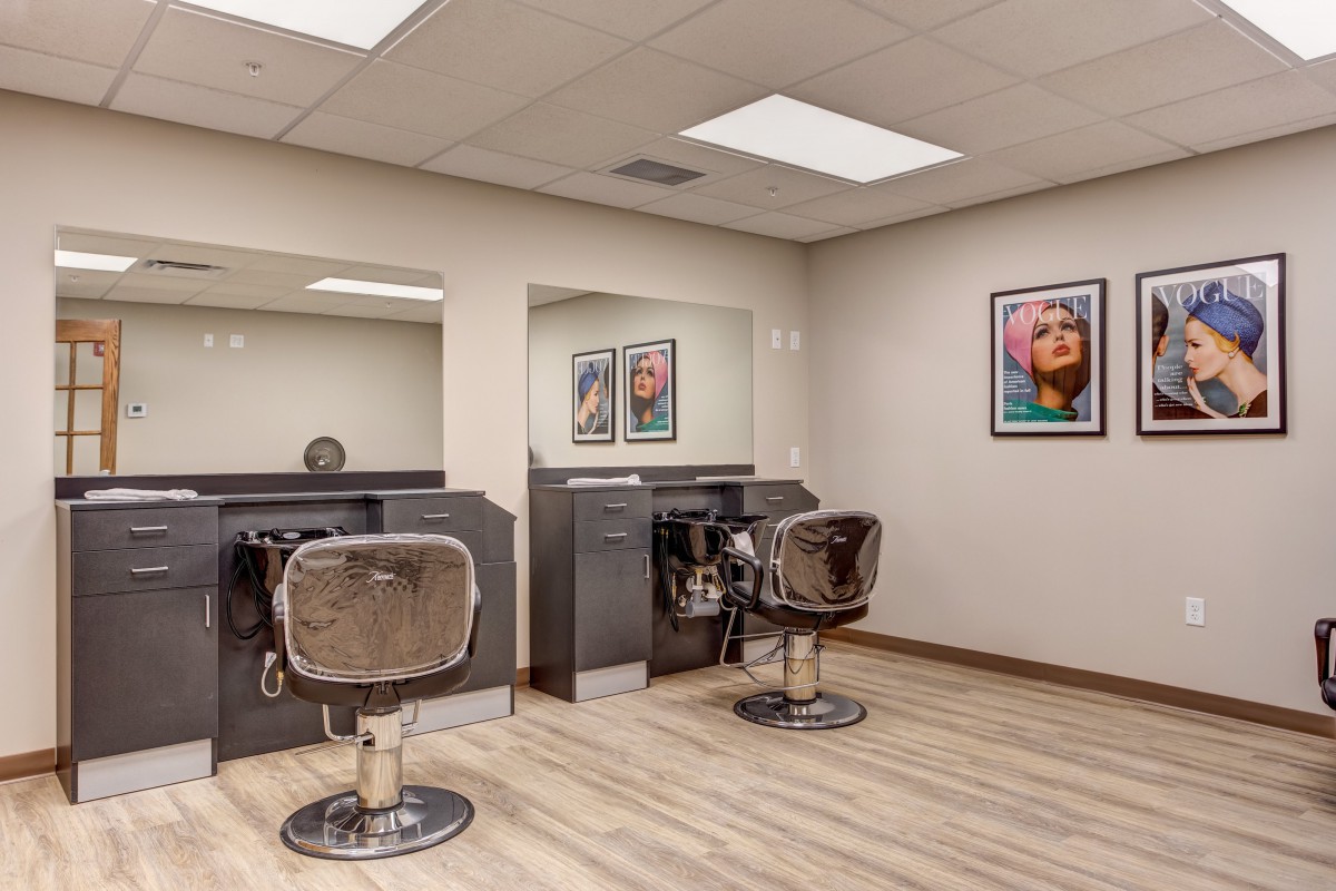 A modern hair salon with two styling stations featuring comfortable chairs, large mirrors, and vibrant wall art.