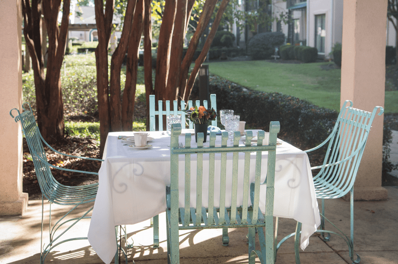 A sunlit outdoor dining area with a table set for breakfast in a garden setting.