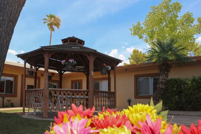 A charming house with a wooden gazebo and colorful flowers in the garden under a clear blue sky.