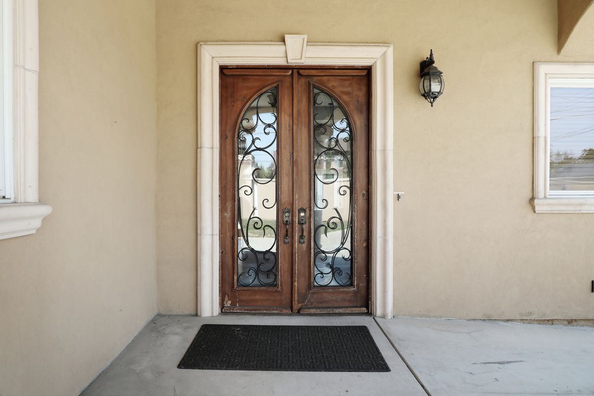 A set of elegant wooden double doors with decorative glass and wrought iron designs, accompanied by an exterior light fixture and a doormat.