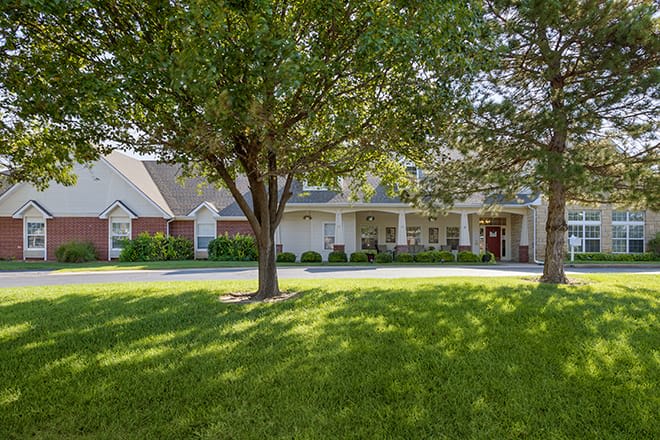 A suburban house with a large tree and well-maintained lawn in the front yard.
