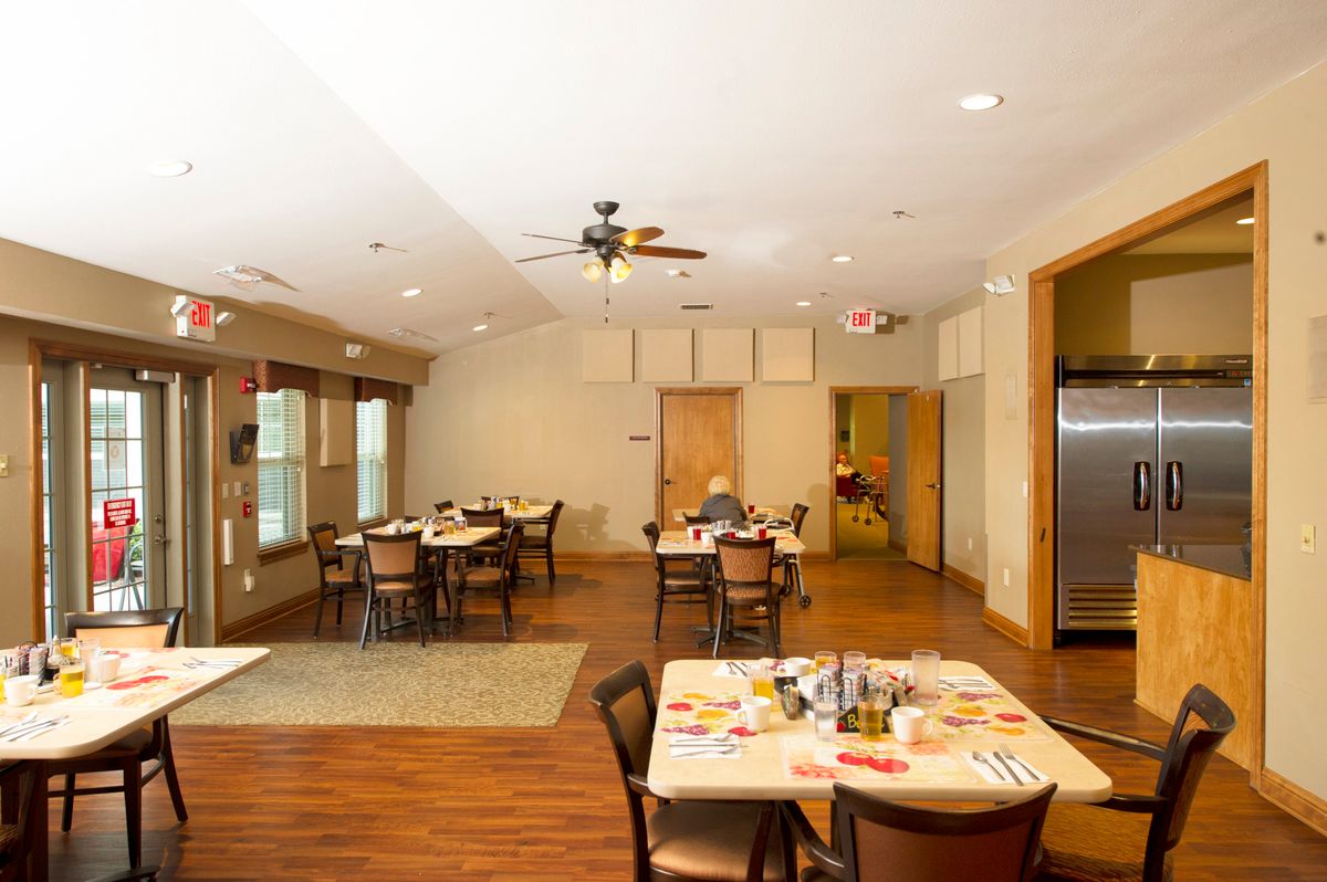 A dining area with multiple tables and chairs, featuring a wooden floor and ceiling fan.