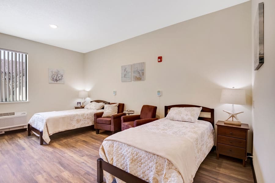 A cozy bedroom with two single beds, two chairs, and warm lighting.