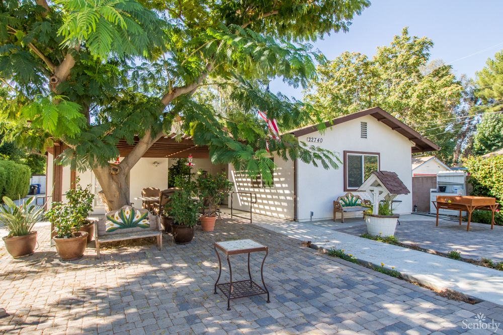 A charming outdoor courtyard with a tree, patio furniture, and a path leading to a house.
