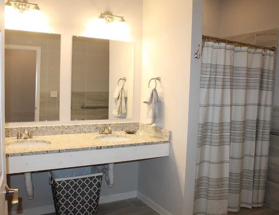 A modern bathroom with a double sink vanity, large mirrors, and a shower area with a striped curtain.