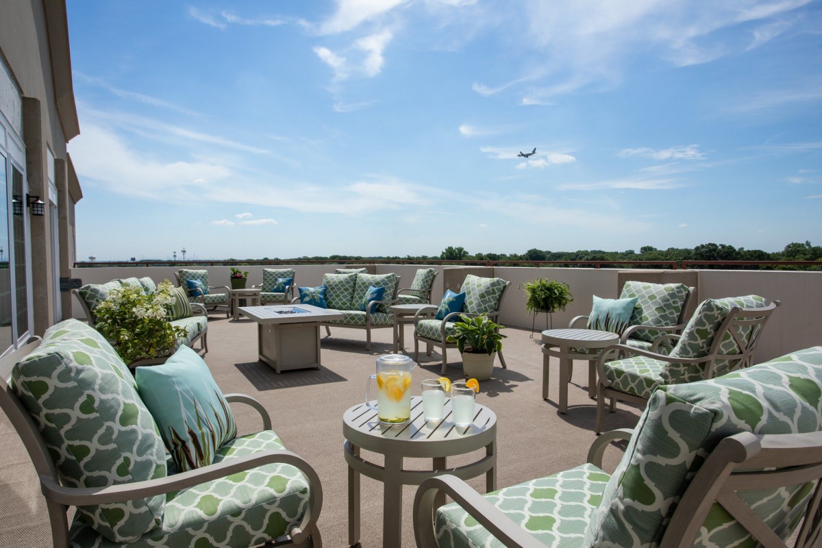 A spacious outdoor patio with comfortable seating and a clear blue sky, featuring a plane flying overhead.