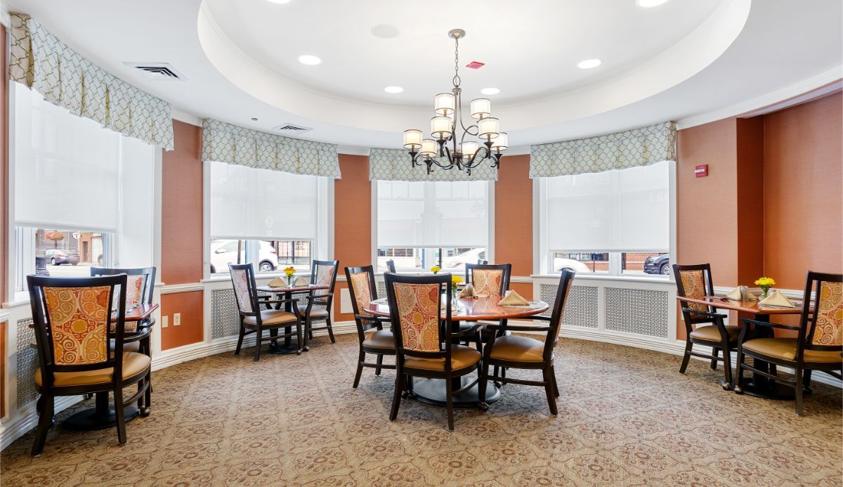 A cozy dining area with a chandelier and multiple tables surrounded by chairs.