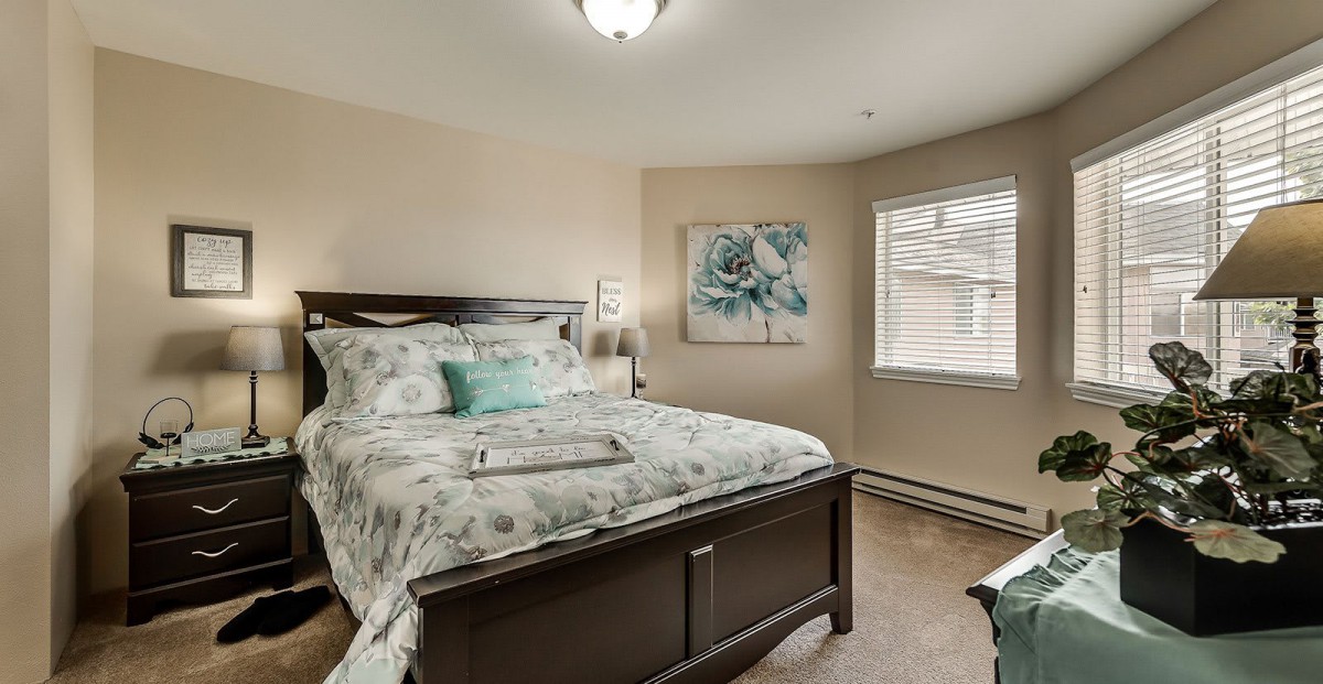 A cozy bedroom with a bed adorned in floral bedding, featuring artwork on the wall and natural light coming through the window.