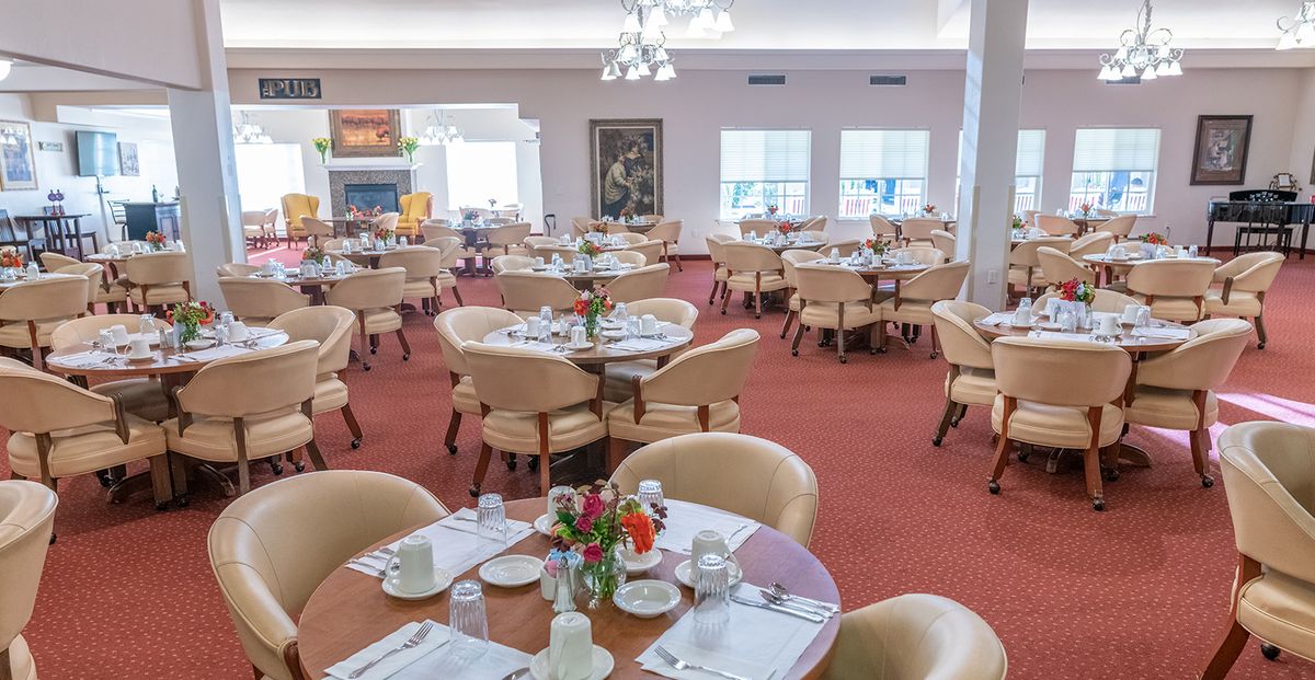 A well-arranged dining area with multiple set tables and chairs, featuring bright natural lighting.