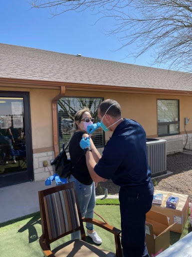 A healthcare professional administering a vaccination to a patient outdoors, both wearing masks for safety.