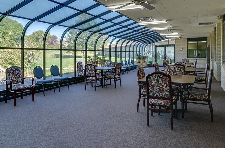 A spacious conservatory with large windows and several tables and chairs under a glass ceiling.