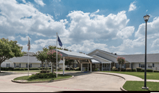 A view of a building entrance with a flagpole, under a partly cloudy sky.