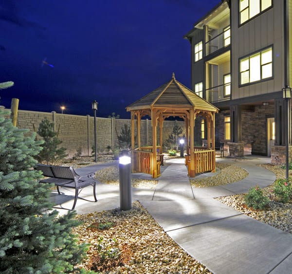 A well-lit garden with a gazebo and pathway at night, next to a building.