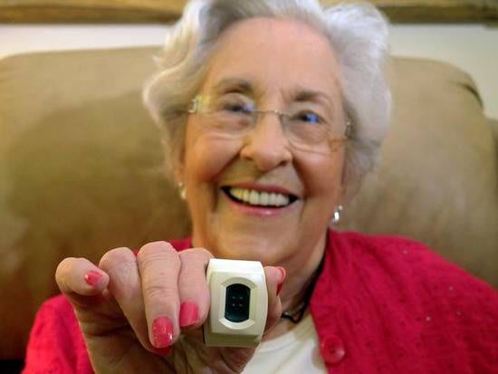 An elderly woman smiling and showing a technological ring-like device.