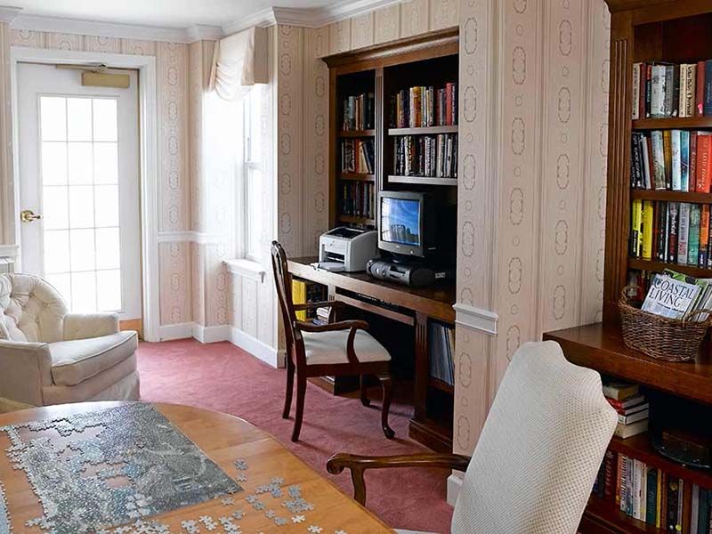 A home office with a desk, computer, and bookshelf next to a window.
