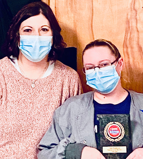 Two individuals proudly holding an award while wearing masks.