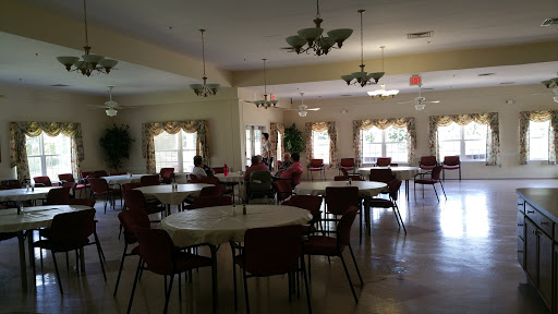 A spacious community dining area with round tables and chairs, illuminated by ceiling lights.