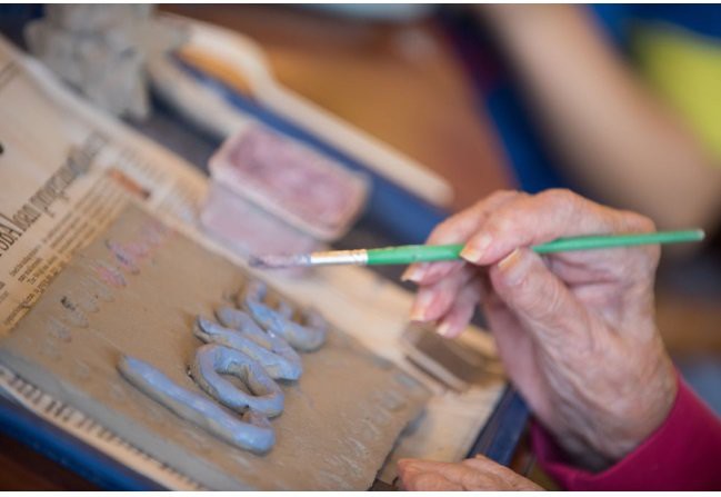 A person painting letters on a clay surface with a brush.