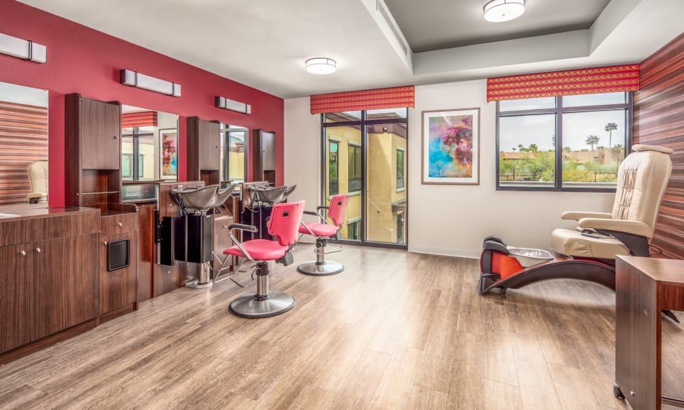 A modern hair salon with sleek wooden flooring, stylish pink chairs, and large mirrors providing a bright and welcoming atmosphere.