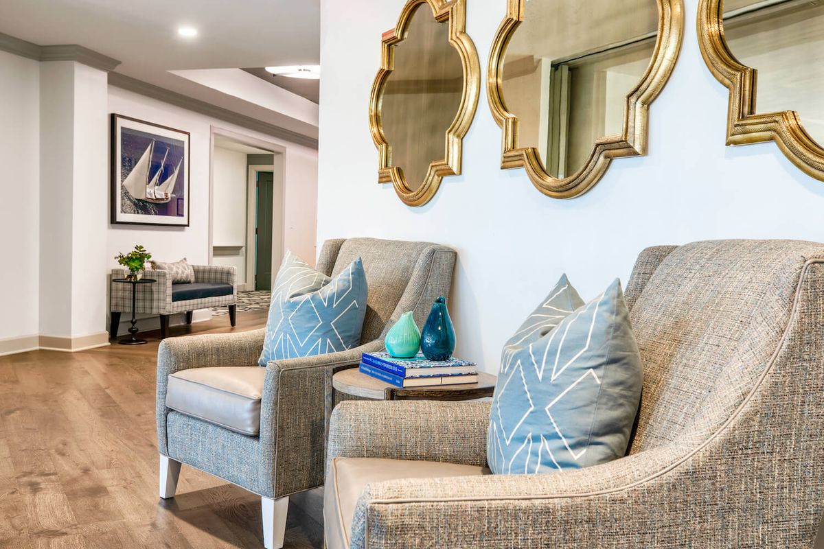 A modern living room with two upholstered chairs, decorative pillows, and stylish mirrors on the wall.