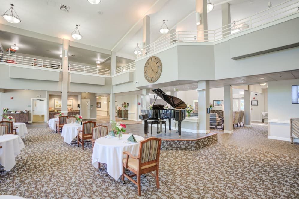 An elegant and spacious dining area featuring a grand piano and neatly arranged tables with white tablecloths.