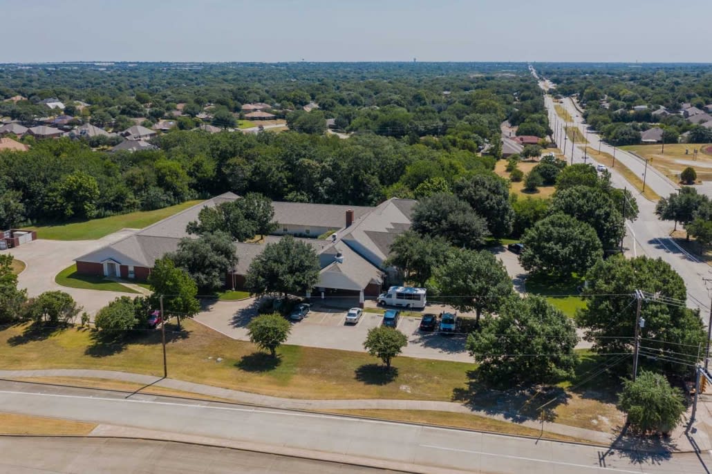 An aerial view of a suburban area featuring a large building surrounded by trees and vehicles in the parking lot.