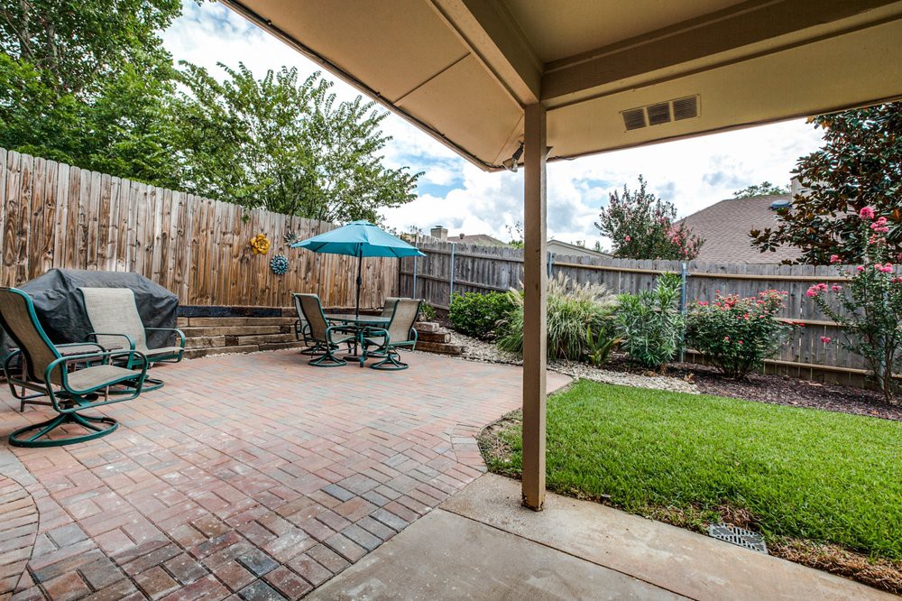 A cozy backyard with a brick patio, featuring outdoor furniture and an umbrella, surrounded by greenery.