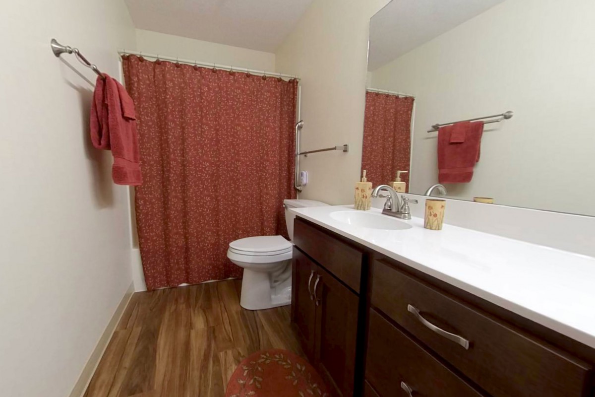 A neatly organized bathroom with a red shower curtain and matching towels.