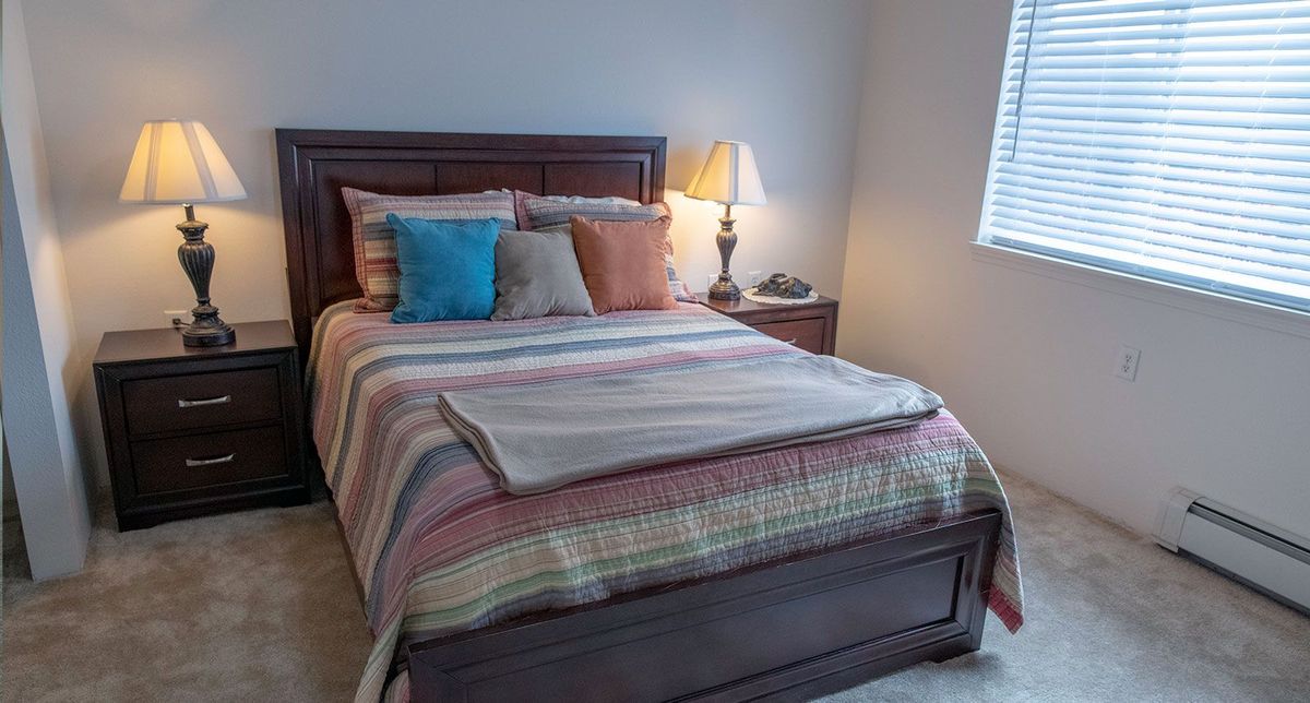 A cozy bedroom with a neatly made bed featuring striped bedding and assorted pillows, accompanied by a nightstand and lamp.