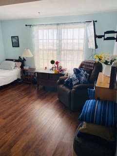A cozy bedroom with an armchair, bed, and desk by a large window.