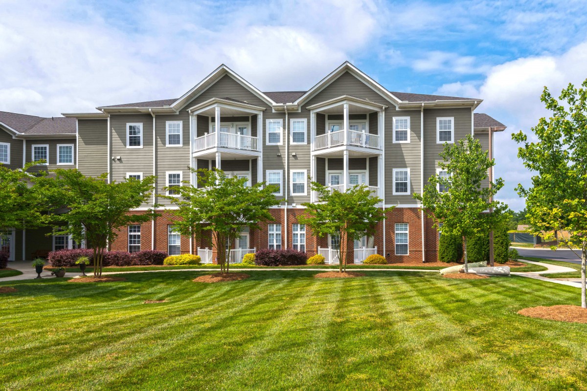 A well-maintained apartment building with a manicured lawn and trees in front.