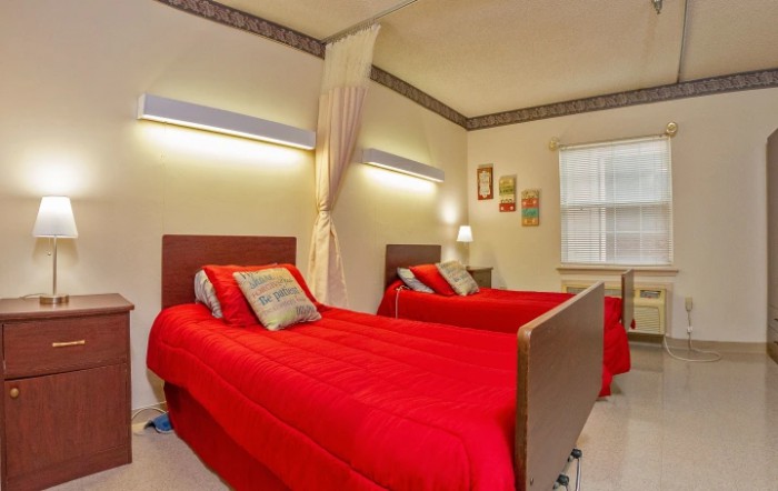 A cozy bedroom with two single beds adorned with red bedspreads, a nightstand between them, and decorative elements on the walls.