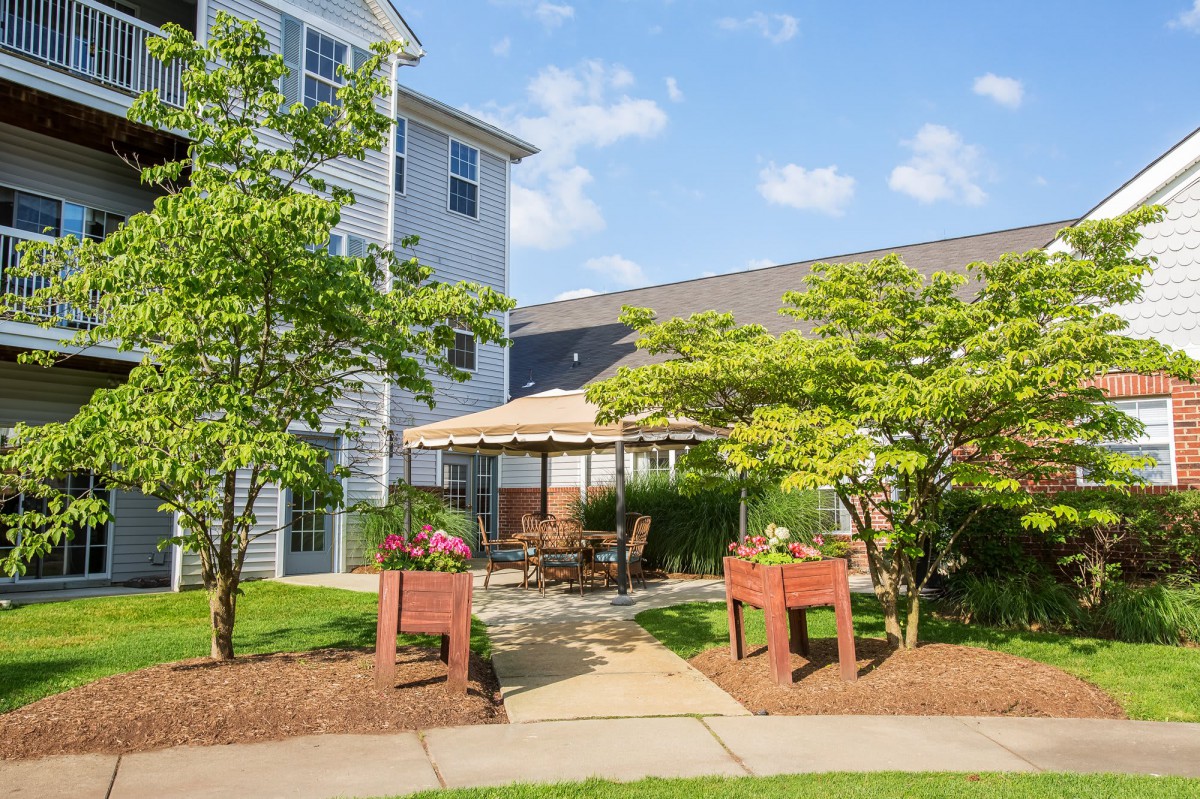 A cozy outdoor patio area surrounded by lush greenery and an apartment building on a sunny day.