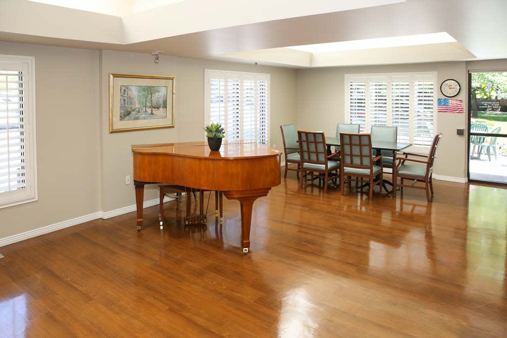 A spacious living room featuring a grand piano and a dining area with hardwood floors.