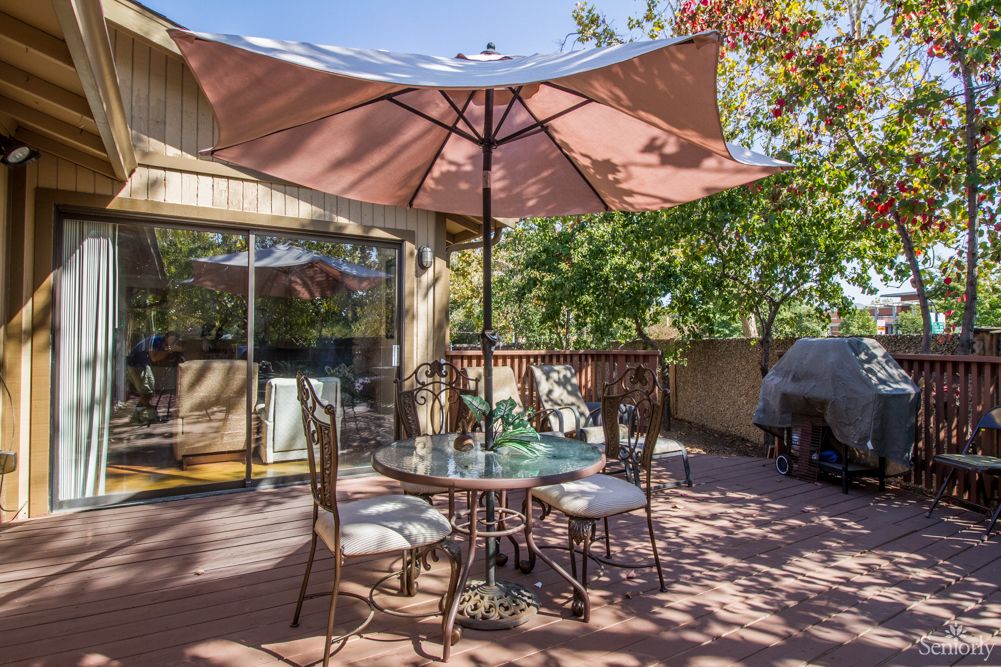 A sunny patio with a table and chairs set under a large umbrella.