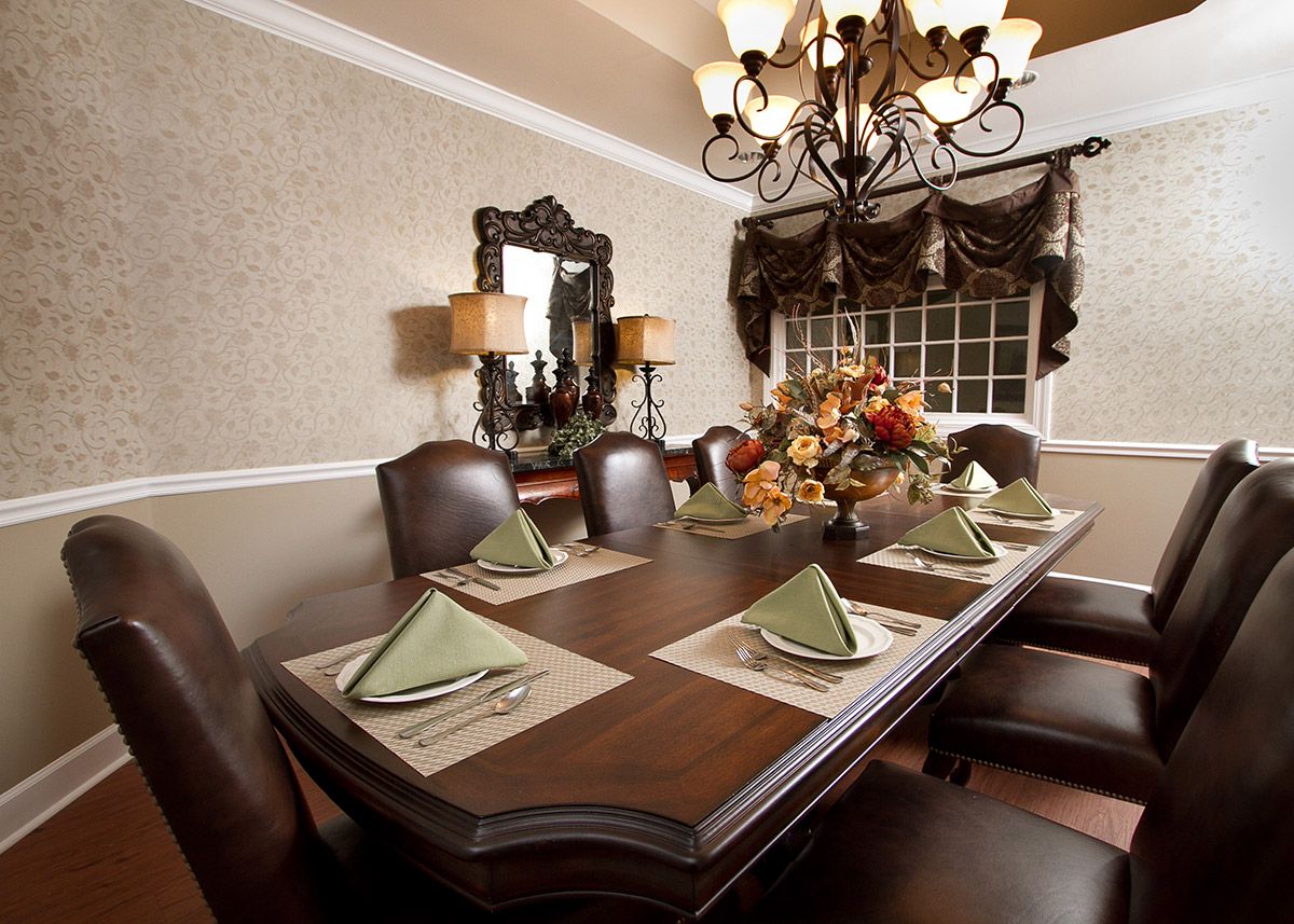 A beautifully set dining room with an elegant table, adorned with folded napkins and a floral centerpiece, under a classic chandelier.