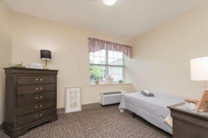 A simple bedroom with a single bed and dresser, featuring a window with curtains.