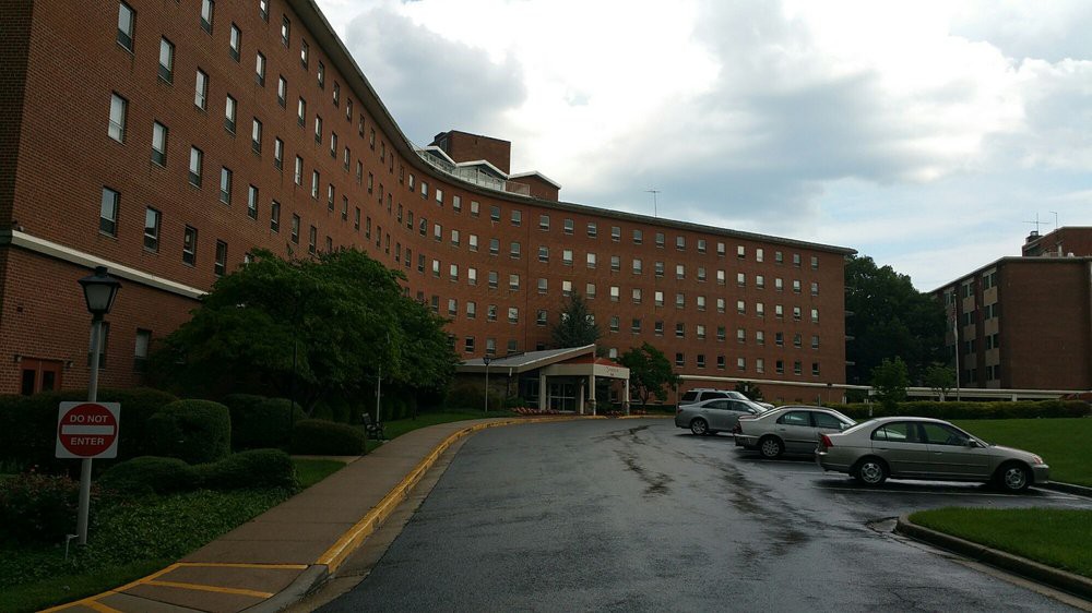 A large brick building with a curved structure, featuring multiple windows and surrounded by a parking lot under a cloudy sky.